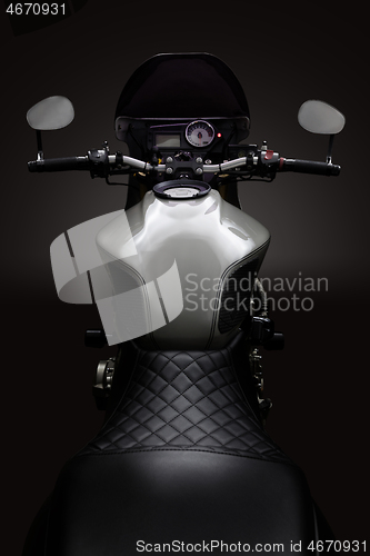 Image of Custom caferacer motorbike on dark background with its headlight on.