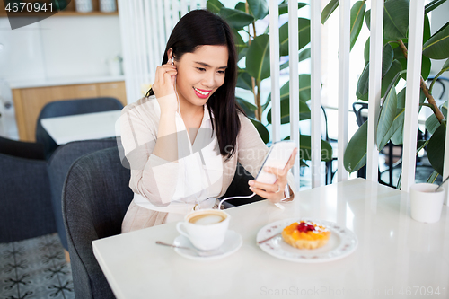 Image of asian woman with smartphone and earphones at cafe