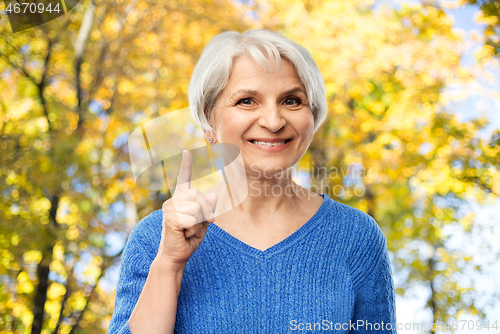 Image of senior woman pointing finger up in autumn park