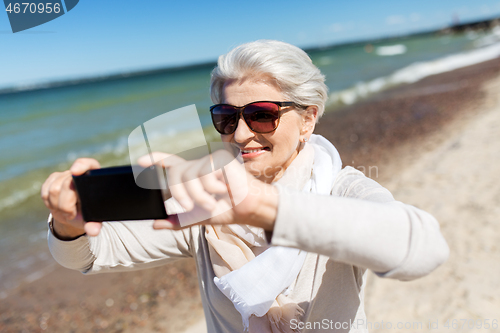 Image of senior woman taking selfie by smartphone on beach