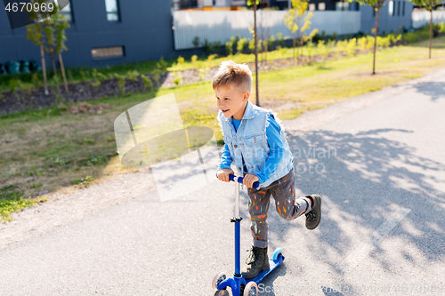 Image of happy little boy riding scooter in city