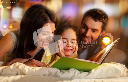 Image of happy family reading book in bed at night at home