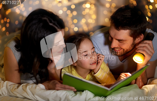 Image of happy family reading book in bed at night at home