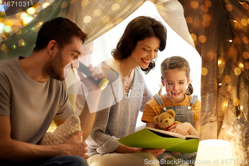 Image of happy family reading book in kids tent at home