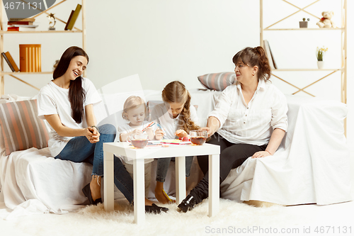Image of Little girls, attractive young mother and charming grandmother are sitting at home