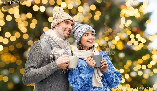 Image of happy couple with mugs over christmas lights