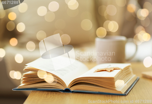 Image of book with autumn leaf on wooden table at home