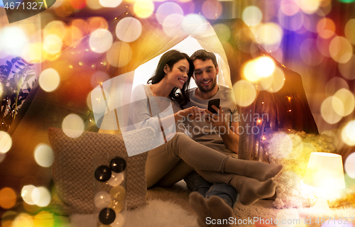 Image of happy couple with smartphone in kids tent at home