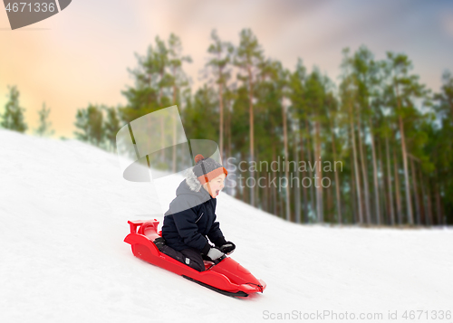 Image of happy boy sliding on sled down snow hill in winter