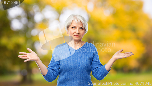 Image of senior woman shrugging in autumn park