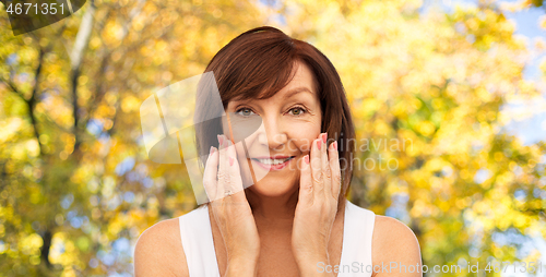 Image of smiling senior woman touching her face in autumn