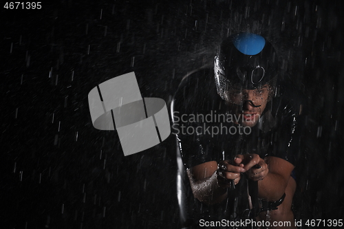 Image of triathlon athlete riding bike fast on rainy night