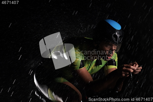 Image of triathlon athlete riding bike fast on rainy night