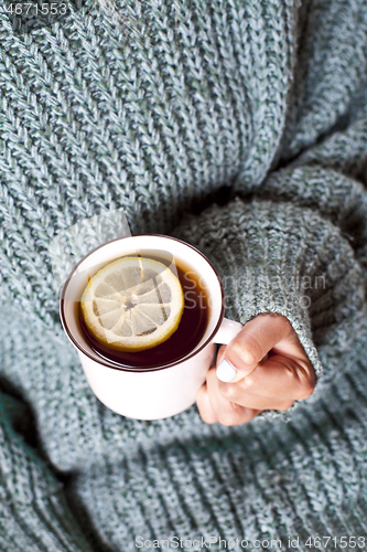 Image of Female hands holding mug of hot tea with lemon in morning.