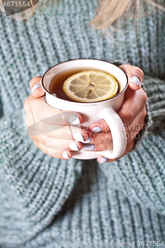 Image of Female hands holding mug of hot tea with lemon in morning.