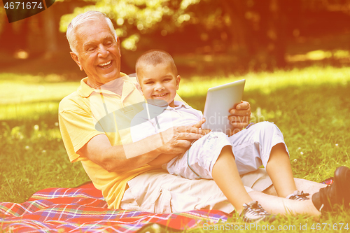 Image of grandfather and child in park using tablet