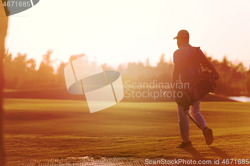 Image of golfer  walking and carrying golf  bag at beautiful sunset