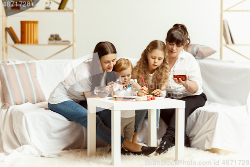 Image of Little girls, attractive young mother and charming grandmother are sitting at home