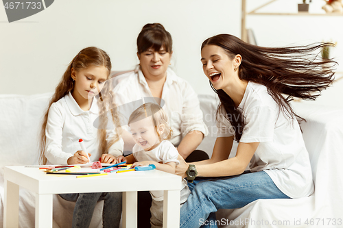 Image of Little girls, attractive young mother and charming grandmother are sitting at home