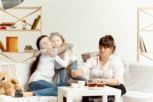 Image of Little girls, attractive young mother and charming grandmother are sitting at home