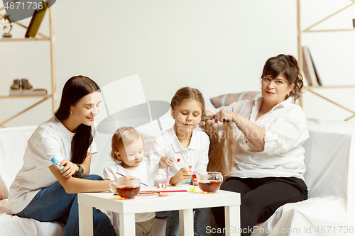 Image of Little girls, attractive young mother and charming grandmother are sitting at home