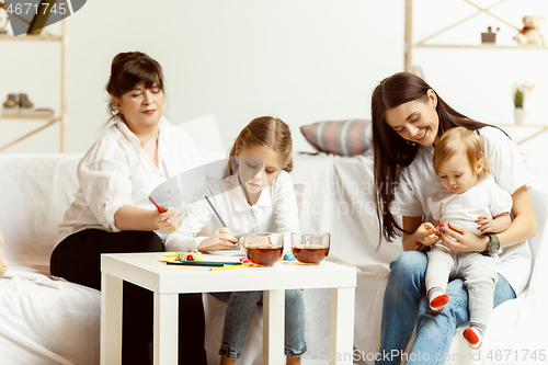 Image of Little girls, attractive young mother and charming grandmother are sitting at home