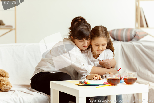 Image of Little girl and charming grandmother are sitting at home