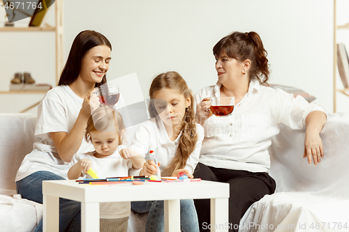 Image of Little girls, attractive young mother and charming grandmother are sitting at home