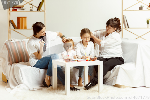 Image of Little girls, attractive young mother and charming grandmother are sitting at home