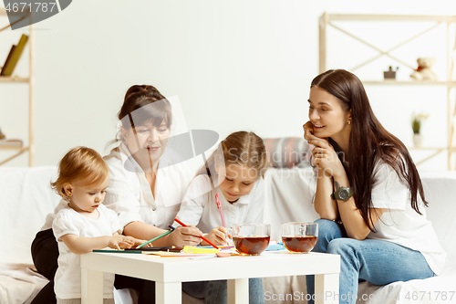 Image of Little girls, attractive young mother and charming grandmother are sitting at home