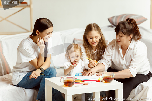 Image of Little girls, attractive young mother and charming grandmother are sitting at home