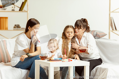 Image of Little girls, attractive young mother and charming grandmother are sitting at home