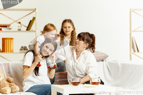 Image of Little girls, attractive young mother and charming grandmother are sitting at home