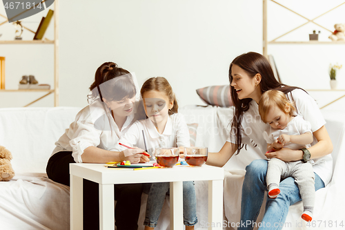 Image of Little girls, attractive young mother and charming grandmother are sitting at home