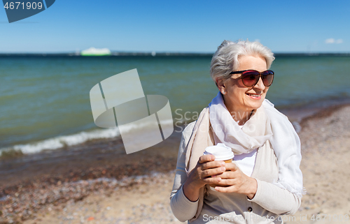 Image of senior woman drinking takeaway coffee on beach