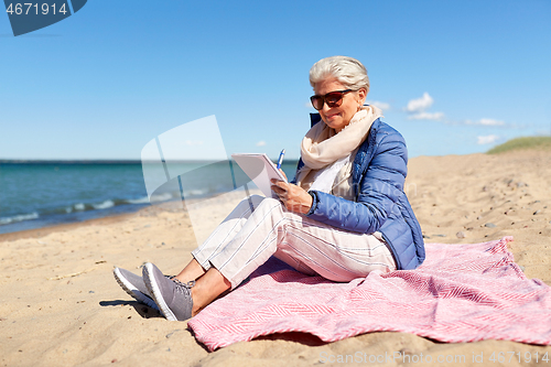 Image of senior woman writing to notebook on summer beach