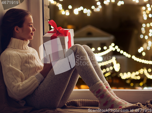 Image of girl with christmas gift sitting on window sill
