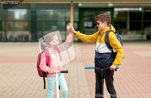 Image of happy school children with backpacks and scooters