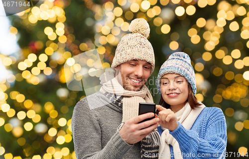 Image of happy couple with smartphone over christmas lights