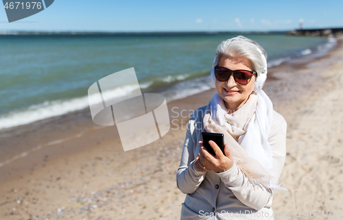 Image of old woman in headphones with smartphone on beach