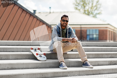 Image of indian man with skateboard sitting on stairs