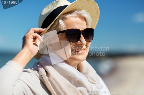 Image of happy senior woman in sunglasses and hat on beach