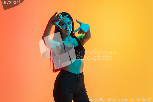 Image of Young woman\'s portrait on yellow-orange studio background in neon light