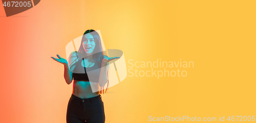 Image of Young woman\'s portrait on yellow-orange studio background in neon light