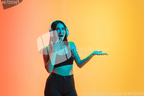 Image of Young woman\'s portrait on yellow-orange studio background in neon light