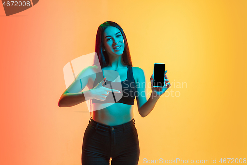 Image of Young woman\'s portrait on yellow-orange studio background in neon light