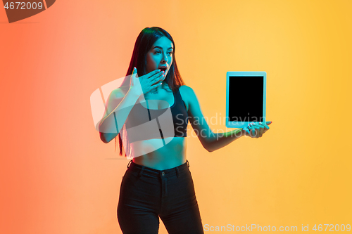 Image of Young woman\'s portrait on yellow-orange studio background in neon light