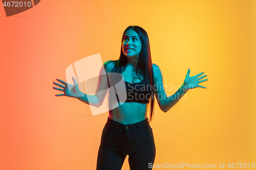 Image of Young woman\'s portrait on yellow-orange studio background in neon light