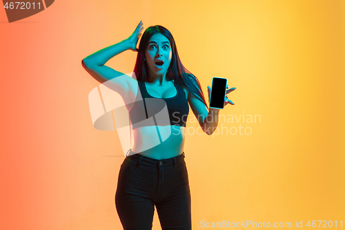 Image of Young woman\'s portrait on yellow-orange studio background in neon light