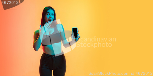 Image of Young woman\'s portrait on yellow-orange studio background in neon light